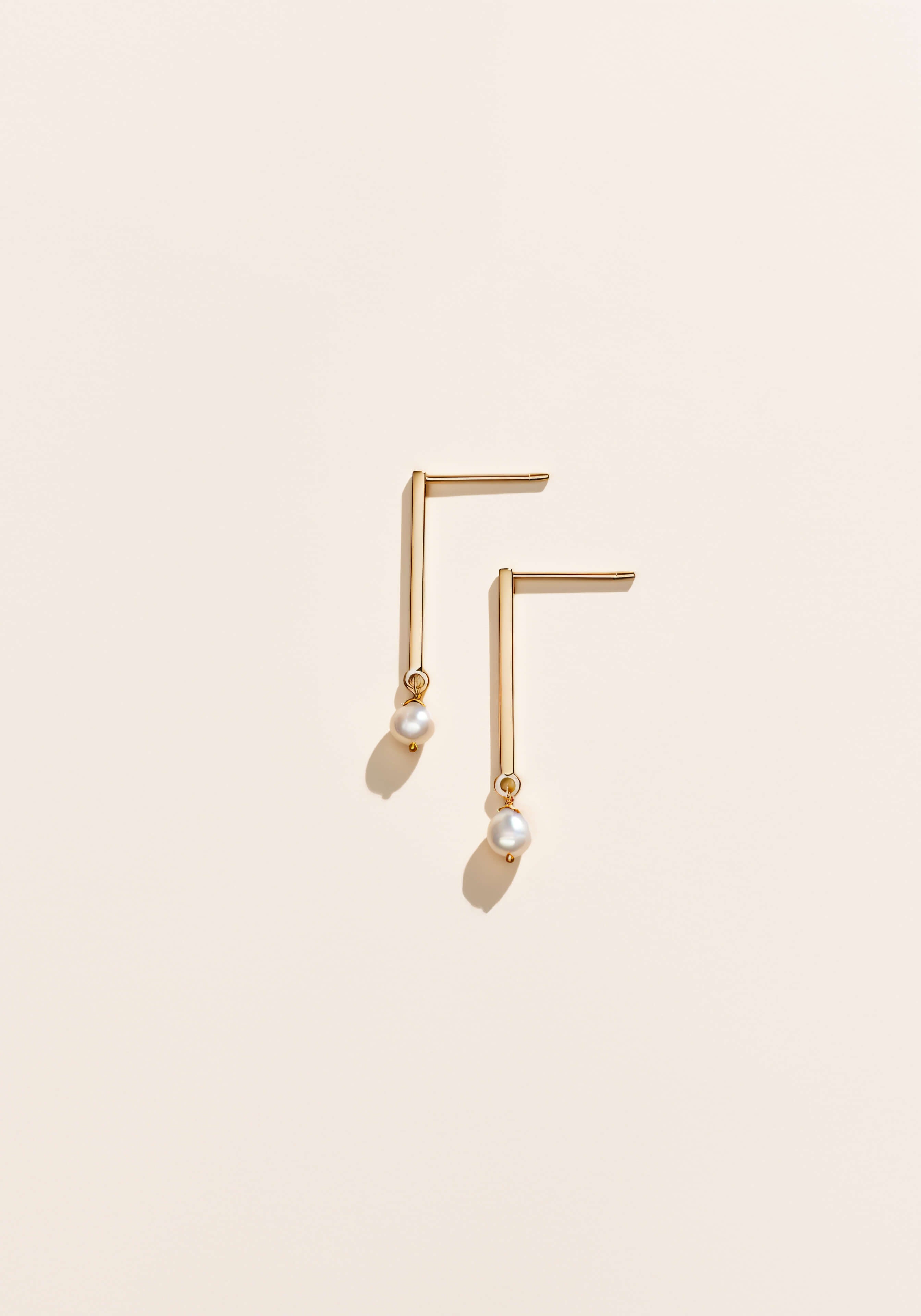 Gold earrings that resemble a thick vertical bar with delicate pearls on the end.