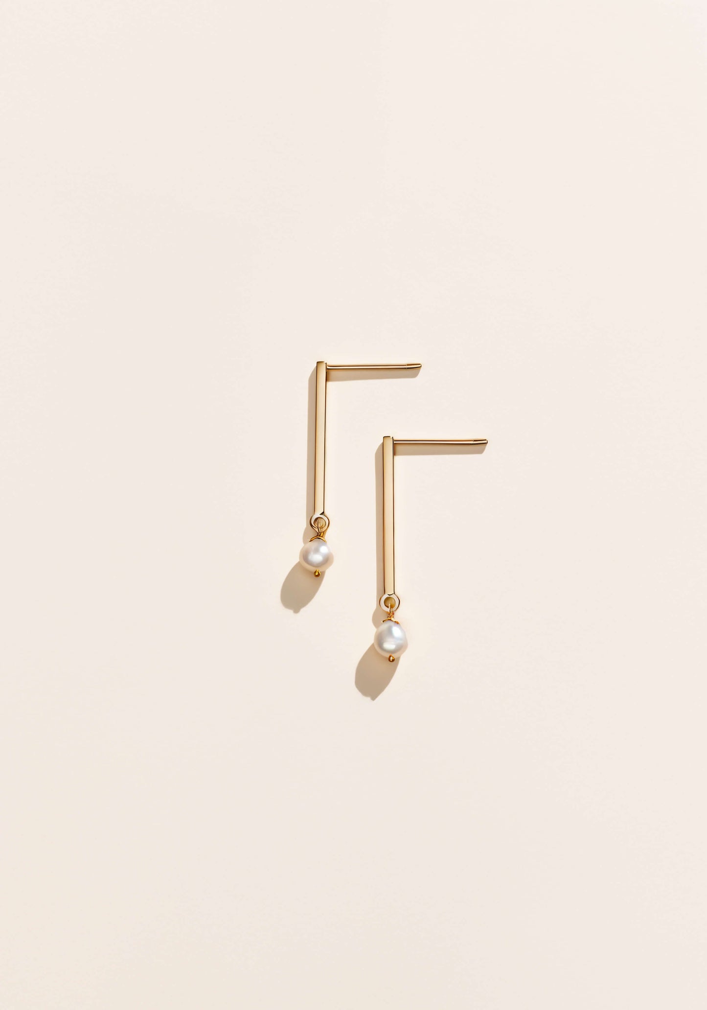Gold earrings that resemble a thick vertical bar with delicate pearls on the end.