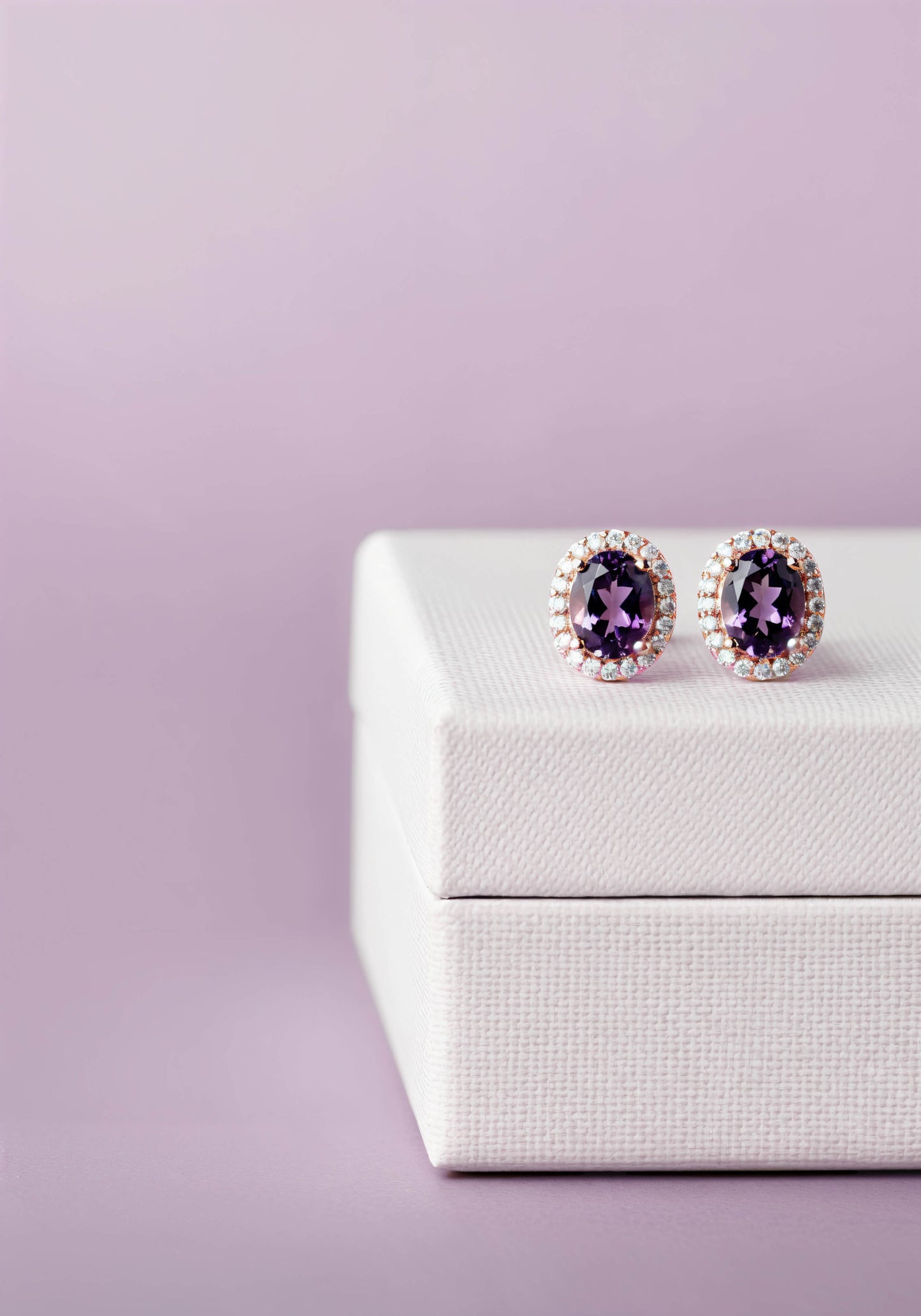 Amethyst earrings with a diamond halo resting on a white jewelry box.